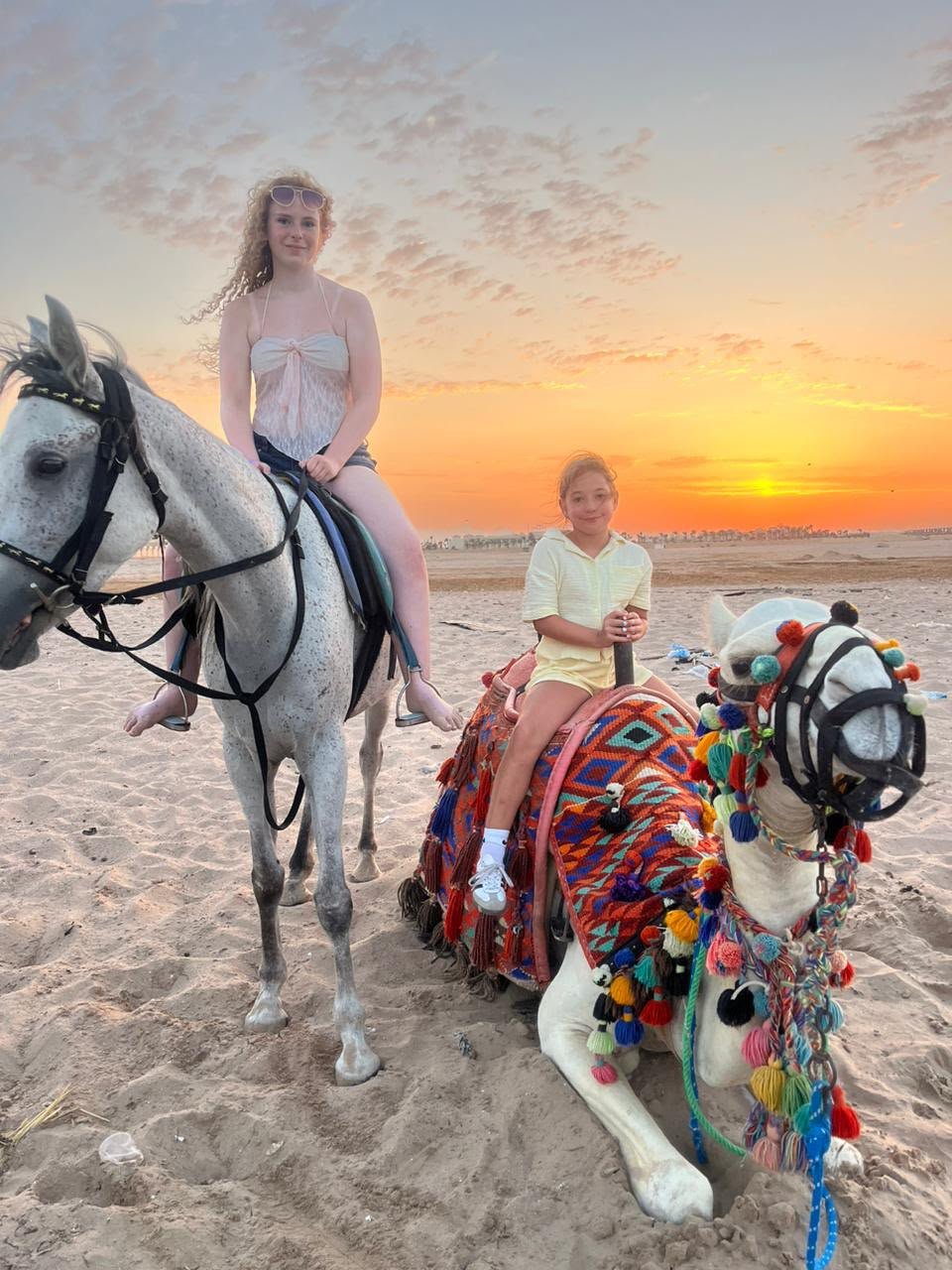 Familie beim Pferde- und Kamelreiten am Strand bei Sonnenuntergang